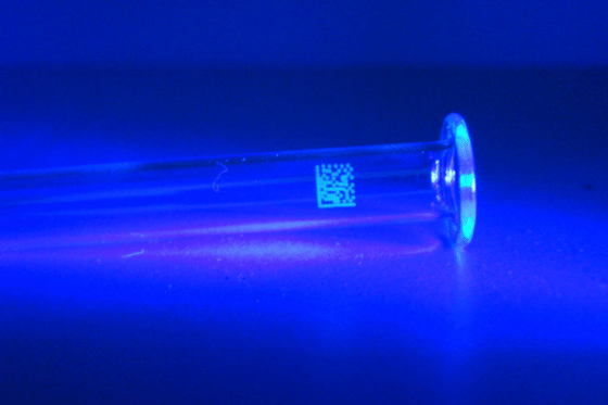 Przemysłowy tester nadruków UV REA JET podczas kontroli jakości kodów świecących na opakowaniu produktu.