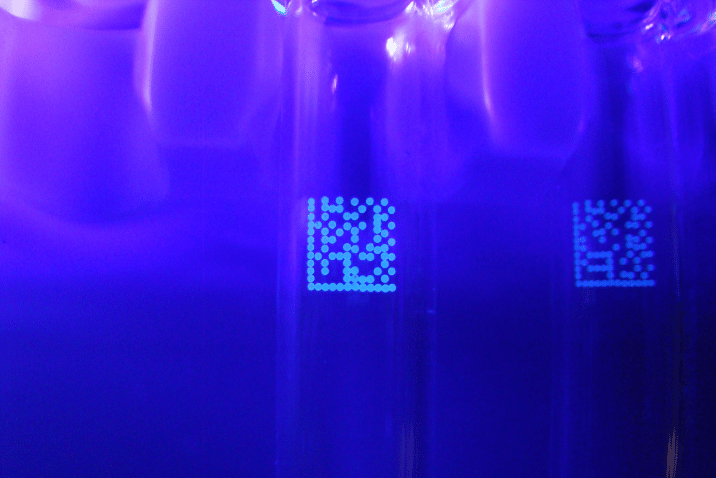 Kody Data Matrix wykonane atramentem fluorescencyjnym REA JET i widoczne w świetle UV na butelkach.