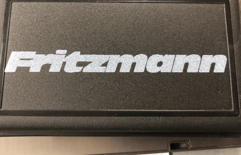 Białe logo Fritzmann nadrukowane na czarnej, teksturowanej powierzchni produktu