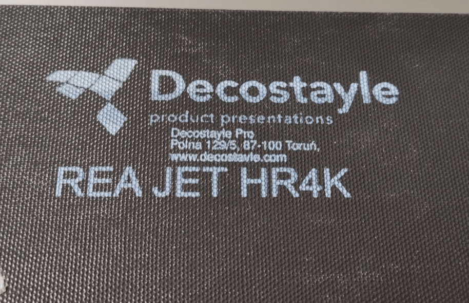 Białe logo Decostayle oraz dane firmy nadrukowane na ciemnym materiale teksturowanym