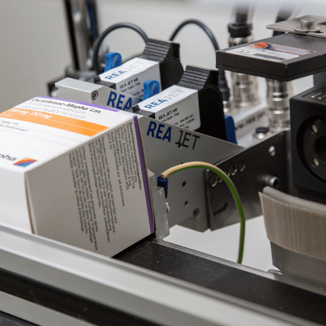 Drukarka REA JET HR nanosząca oznaczenia bezpośrednio na karton przesuwający się na linii produkcyjnej.