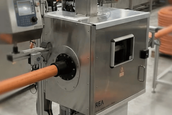 Pomarańczowa rura przechodząca przez system REA ExtruMark 200 na linii produkcyjnej