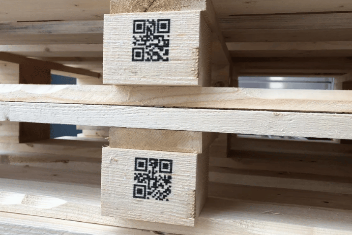 Paleta drewniana z wydrukowanymi kodami QR na dwóch klockach nośnych.