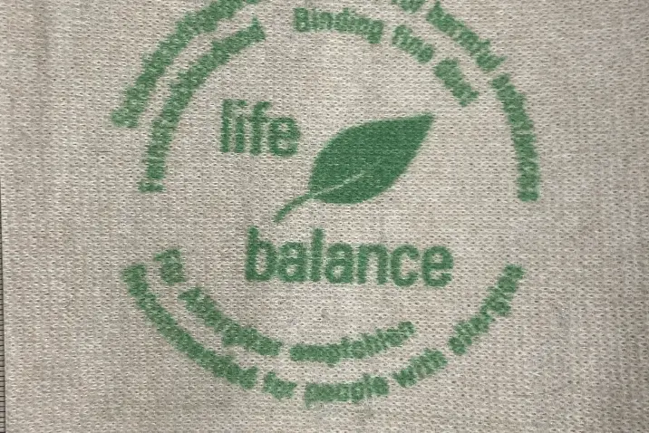 Zielony nadruk logo life balance z motywem liścia na jasnym materiale tekstylnym o wyraźnej strukturze włókien.