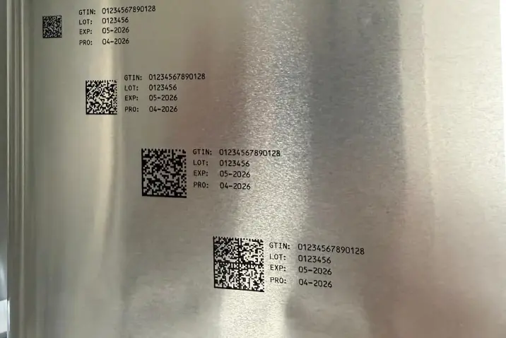Zbliżenie na nadruk REA JET UP na jasnej folii opakowaniowej z drobnymi tekstami, kodami 2D i symbolami.